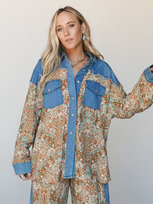 An oversized button-down shirt in a warm brown paisley print with denim yoke, cuffs, and chest pockets — worn as a set with matching wide-leg pants, giving off that effortless vintage-western energy.