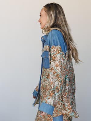 A side-profile shot of a model in a mixed-media jacket that pairs a denim upper with a flowing paisley-printed lower half — the kind of piece that feels like it was always yours.