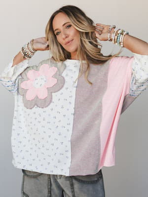 A relaxed, oversized mixed-print top in soft pastels — floral ditsy, stripe panels, and a bold flower appliqué — styled with stacked beaded bracelets and washed cargo pants for that effortlessly expressive, lived-in kind of vibe.