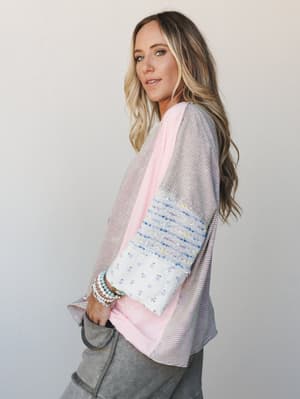 A relaxed mixed-media top shot in profile, layering pink and gray pinstripes with a patchwork sleeve detail in periwinkle boucle and ivory floral — the kind of top that looks effortless but has a lot going on in the best way.