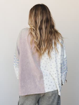 A back-facing shot of a mixed-fabric top with a patchwork feel — one half striped pink and cream, the other a soft ivory ditsy floral — paired with grey bottoms against a clean studio wall.