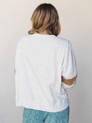 Shot from the back, this relaxed short-sleeve sweatshirt in light heather gray shows off its personality through contrast sleeve panels — a warm tan stripe and a peek of floral fabric at the elbow, paired with floral bottoms just visible at the hem.