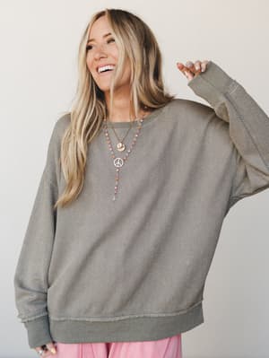 A relaxed, oversized textured sweatshirt in ash olive styled with layered boho necklaces and soft pink pants — the kind of effortless top that looks like you just threw it on and somehow nailed it.