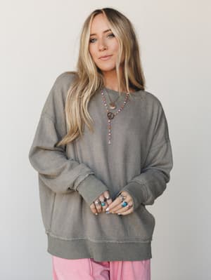 An oversized waffle-knit pullover in washed olive pairs with soft pink wide-leg pants and a stack of boho jewelry — the kind of effortless layered look that feels put-together without trying.