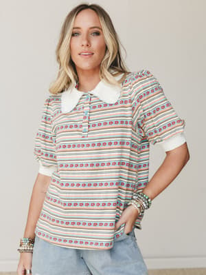 A striped floral-print top with a contrast white Peter Pan collar and puff sleeves, styled with light wash jeans and stacked bead bracelets — the kind of top that looks like it was found in a vintage shop but fits like it was made for you.
