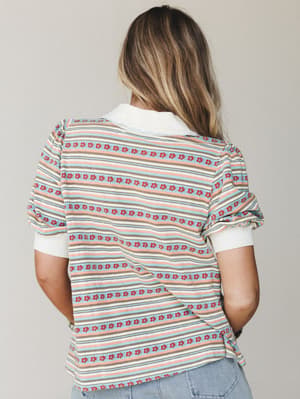 Shot from behind, a striped floral-print collared top in soft sky blue, blush, and taupe pairs with light wash denim — retro-sweet and easy, like something you'd find at the back of a vintage shop and wear on repeat.
