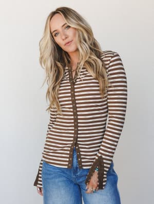A brown and cream striped long-sleeve henley top styled with blue jeans — the kind of easy, put-together look that works just as well for a coffee run as it does for a casual dinner out.