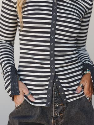A close-up torso shot of a navy and cream striped long-sleeve henley top with a snap-button placket down the center front, styled with dark wash wide-leg jeans and layered jewelry for an easy, lived-in look.