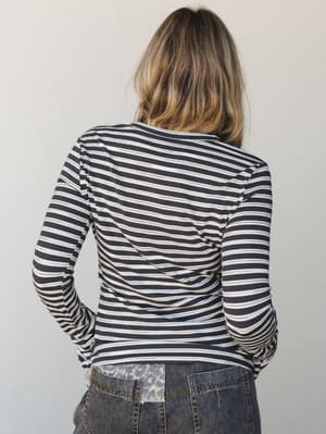 A back-view shot of a fitted long-sleeve striped top in navy and cream, paired with distressed denim — the kind of effortless layering piece that works as hard as she does.