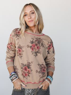 A floral sweatshirt in a warm toasty tan gets the vintage treatment — rose bouquet print, contrast stitch detail, and a stack of beaded bracelets that look like they were collected, not coordinated.