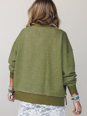 A relaxed, oversized olive sweatshirt shot from the back, layered over a white lace skirt — the raw-hem details and stacked boho bracelets giving it that effortlessly lived-in feel.
