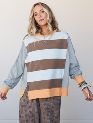 An oversized colorblock sweatshirt top in powder blue and mocha wide stripes with fine-striped sleeves and peach ribbed trim, styled with printed wide-leg pants and layered jewelry for an effortlessly relaxed, personality-forward look.