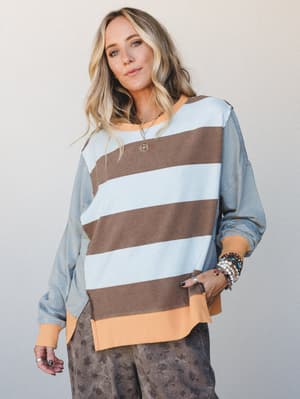 A relaxed, mixed-print sweatshirt top with wide body stripes and fine-striped sleeves in dusty blue, warm brown, and peach — styled with stacked boho jewelry and floral joggers for an effortlessly collected everyday look.