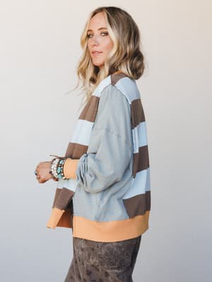 A relaxed oversized pullover top in color-blocked wide stripes and a fine-stripe contrast sleeve, styled with star-print pants and stacked boho bracelets — the kind of top that makes a Tuesday feel a little more like itself.