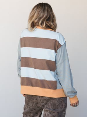 A back-view shot of a mixed-stripe pullover top with a relaxed, lived-in feel — wide horizontal stripes on the body contrast with fine pinstripes on the sleeves, finished with a warm peach ribbed hem that ties the whole thing together.
