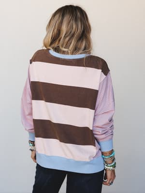 A relaxed mixed-stripe sweatshirt in chocolate, blush, and sky blue worn from the back, stacked with turquoise and beaded bracelets — the kind of top that looks intentional without trying.