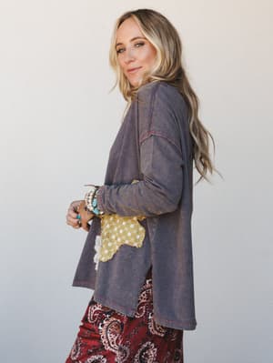 A relaxed side-profile shot of a model in a washed ash longline top with a patchwork appliqué detail, layered over a rich burgundy paisley skirt — the whole look reads like a Saturday that turned into something.