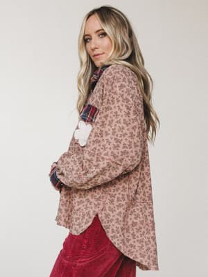 A relaxed floral top in dusty mauve is styled with deep red corduroy pants and a plaid underlayer peeking through — the kind of effortlessly layered look that feels like it came together on purpose, even when it didn't.