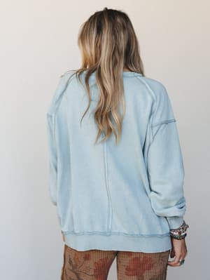 Shot from the back, this washed dusty blue pullover sweatshirt has an effortlessly lived-in feel — paired with printed wide-leg pants and stacked boho bracelets, it reads like a weekend morning that got stylish without trying.