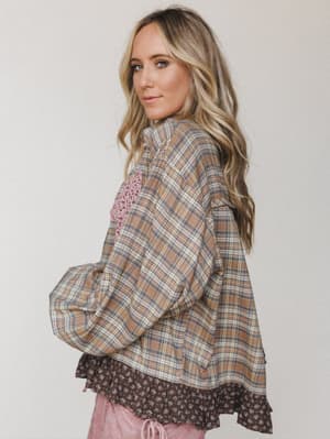 A relaxed plaid oversized top shot from the back-angle, styled with a floral ruffle underlayer and dusty pink pants — the kind of effortless layered look that feels pulled-together without trying.