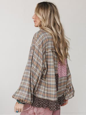 A relaxed patchwork top in warm khaki plaid gets an unexpected twist with mixed fabric panels — eyelet, floral, and plaid — shot from the back to show off the billowy balloon sleeves and layered hem detail.