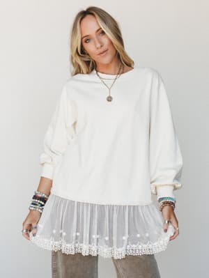A cream sweatshirt top with a dreamy tulle and lace hem extension styled with layered gold necklaces and stacks of colorful beaded bracelets — the kind of piece that looks like it couldn't decide between cozy and romantic, and chose both.