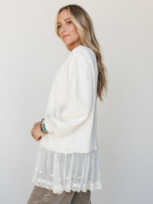 A cream sweatshirt top with a dreamy tulle and lace hem extension is styled with taupe corduroy pants and stacked turquoise jewelry — the kind of outfit that looks effortless but very much on purpose.