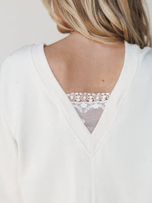 A close-up back shot of a cream knit top with a V-back neckline, revealing a delicate lace and mesh inset panel — the kind of quiet detail that makes a simple top feel like a little secret.