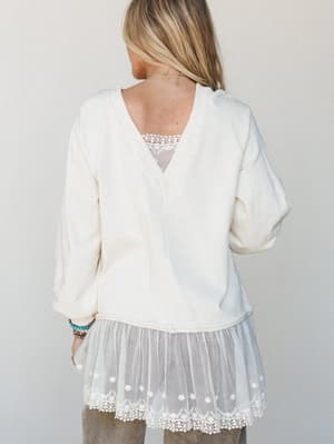 Shot from the back, this ivory knit top pairs relaxed long sleeves with a dreamy tulle and lace hem extension — the kind of piece that looks like it's been in someone's closet forever, in the best way.
