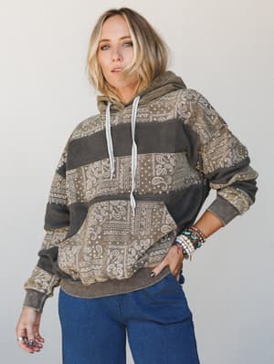 A relaxed bandana-print patchwork hoodie in faded olive and charcoal stripes, styled with wide-leg denim and a stack of boho bracelets — the kind of piece that looks like it's been lived in for years and is better for it.