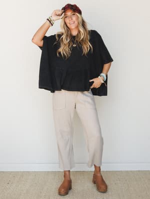 An oversized washed black ruffle-hem top styled with oatmeal textured joggers, platform clogs, and a plaid newsboy cap — the kind of effortlessly put-together look that feels as comfortable as it looks.