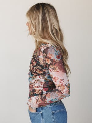 A side profile shot of a long-sleeve floral mesh top styled with medium-wash denim, the mixed floral patchwork print feeling like something you'd find in a vintage shop and immediately never take off.