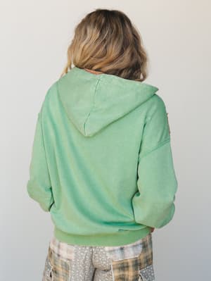 A back-view shot of a model wearing an oversized mint green hoodie with a lived-in, washed finish, paired with patchwork plaid shorts — the kind of outfit that looks effortless because it actually is.