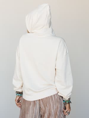 A back-view shot of a cream hoodie styled with striped wide-leg pants and stacked boho bracelets — the kind of effortless outfit that somehow looks intentional every time.