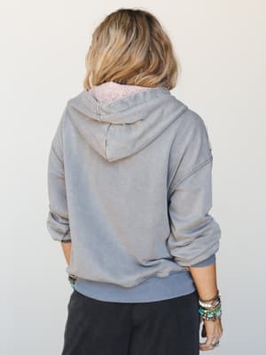 A back-facing shot of a washed grey-blue hoodie styled with dark wide-leg pants and stacked turquoise and silver bracelets — lived-in and relaxed, the kind of hoodie that earns its keep on a coffee run or a lazy Sunday with friends.