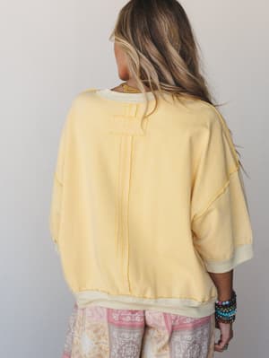 Shot from the back, this soft banana-yellow oversized sweatshirt top has an easy, lived-in feel — styled with paisley bottoms and a stack of boho bracelets that do all the talking.