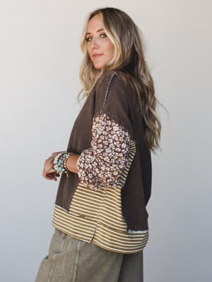 A model shot from a three-quarter back angle showing a mixed-media patchwork top in earthy coffee tones, styled with olive cargo pants and layered turquoise and silver bracelets — the kind of outfit that looks effortless but clearly has opinions.