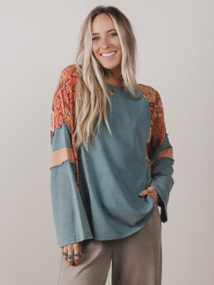 Woman wearing a teal sweater with patterned sleeves against a plain background
