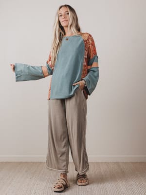 Woman wearing a blue and patterned top with beige pants against a plain background