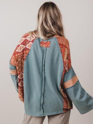 Person wearing a teal jacket with patterned sleeves and back on a plain background