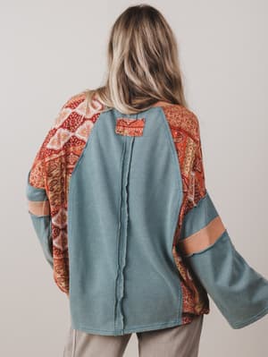 Person wearing a teal jacket with patterned sleeves and back on a plain background