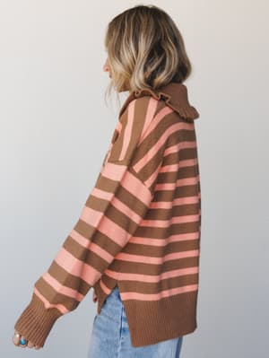 A side-profile shot of a striped knit sweater in warm camel and peachy pink, styled with light wash jeans — the kind of cozy, throwback combo that makes a Tuesday feel intentional.