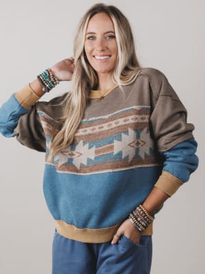 Woman wearing a patterned sweater with blue sleeves and beige accents on a plain background