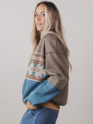 Woman wearing a brown sweater with a pattern and blue sleeves on a plain background
