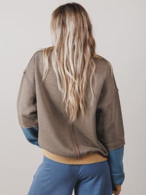 Person wearing a brown jacket with blue sleeves and pants on a plain background