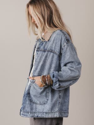 Person wearing an oversized denim jacket against a plain background