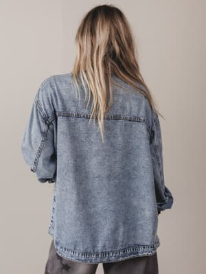 Person wearing a denim jacket from behind on a plain background