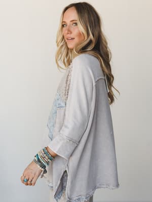A side-profile shot of a model in a relaxed, mixed-fabric thermal top with a patchwork star detail, styled with stacked boho bracelets and denim shorts — the kind of effortless outfit that looks like it came together in two minutes and somehow still
