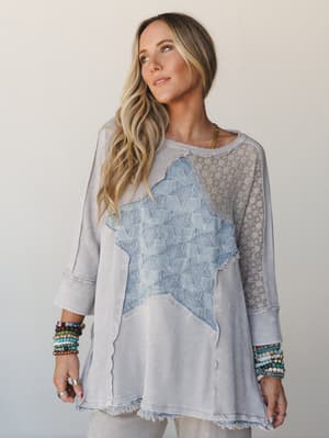 A relaxed, mixed-media thermal top in washed light ash with a large denim star appliqué at the center, lace mesh shoulder panels, and raw-edge seaming — styled with stacked beaded bracelets for that effortlessly collected boho feel.