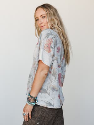 A relaxed floral waffle-knit top in soft grey with faded vintage blooms, styled with stacked turquoise bracelets and leopard print bottoms for that effortless, layered-with-personality kind of look.